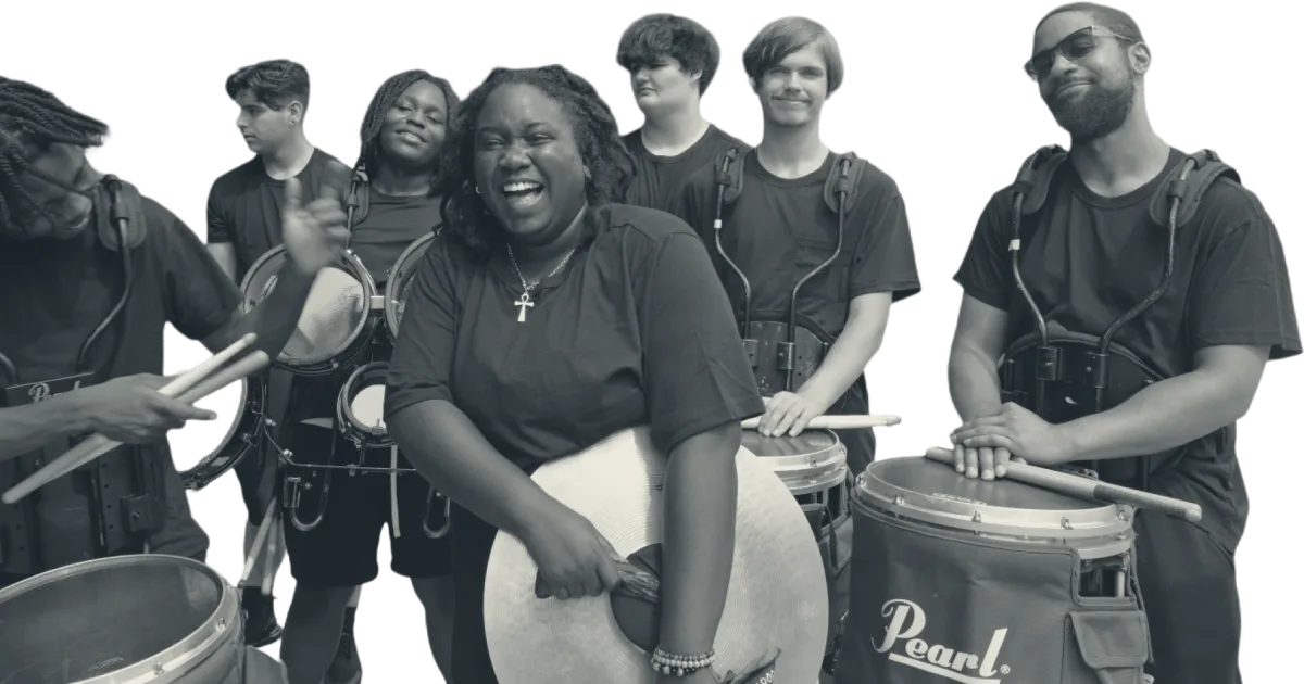 A drumline laughing together, sticks and cymbals in hand.